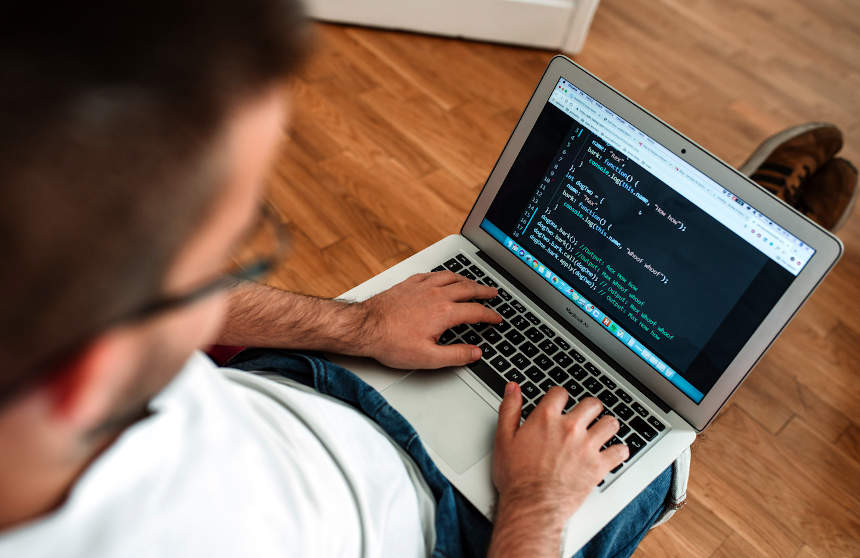 A man is sitting on a wooden floor with a laptop, featuring Choose My Site Digital Marketing and aligning with data-driven online marketing solutions.